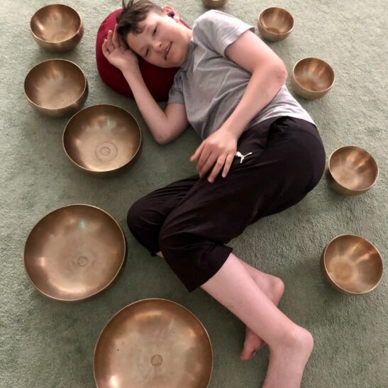 Ein Junge am Boden liegend in mitten von Klangschalen